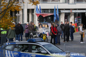 Auf der Versammlungsfäche stehen Menschen, ein Lautsprecherwagen. Ein halb verdecktes Banner mit der Aufschrift »STOPPT den GenderWahn«