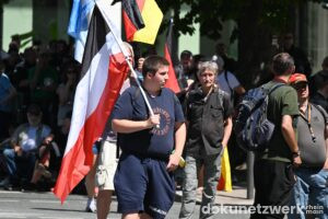 Als der Demozug durch die Blockade ins Stocken gerät, packen Teilnehmende schwarz-weiß-rote Flaggen aus